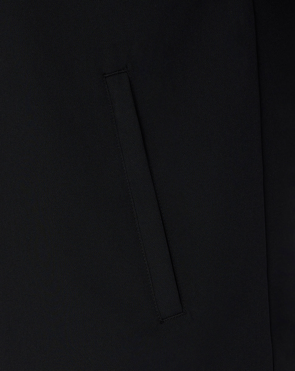 Close-up detail of a black fabric garment showing a vertical welt pocket and smooth matte texture.