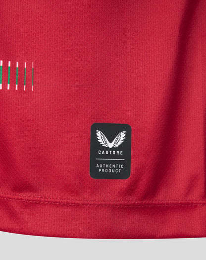 Close-up of a red athletic garment showing a black Castore Authentic Product label sewn onto the lower front, with a small striped detail on the upper left.