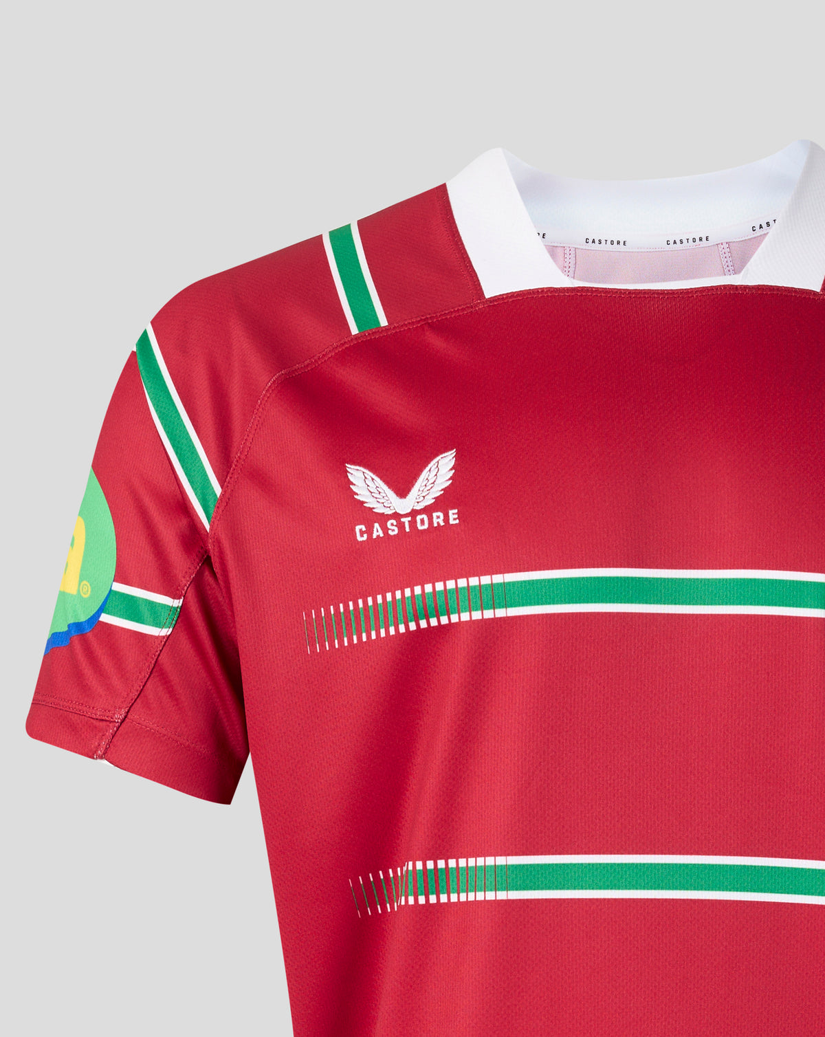 A close-up of a red short-sleeve sports jersey with green and white stripes, featuring the white Castore wing logo on the chest.