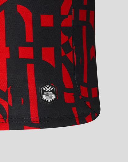 Close-up of a black athletic shorts leg featuring a bold red abstract geometric pattern and a white Umbro logo patch near the hem, set against a light gray background.