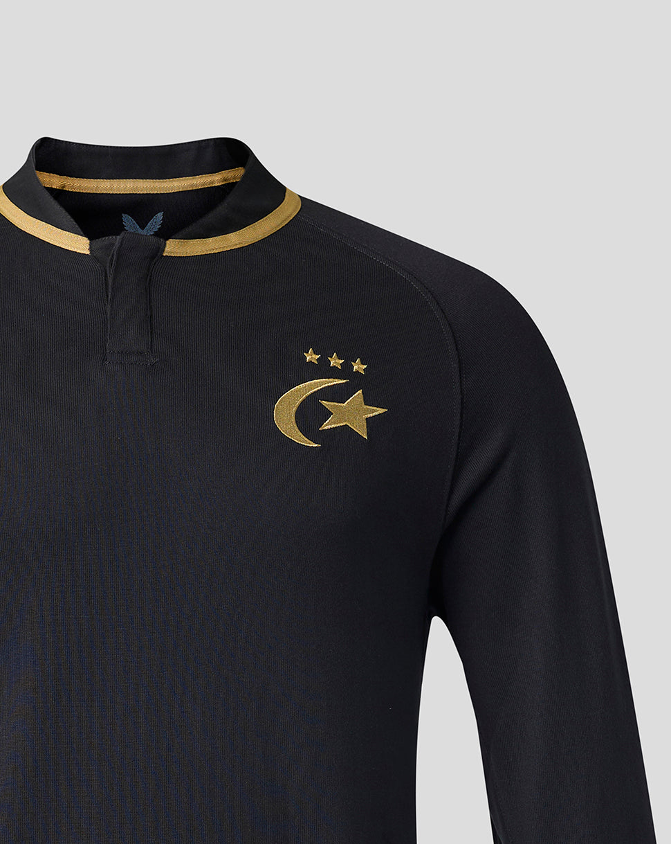A close-up of a black long-sleeve athletic top with a gold collar trim and a gold crescent and star emblem with three stars on the left chest, set against a light gray background.