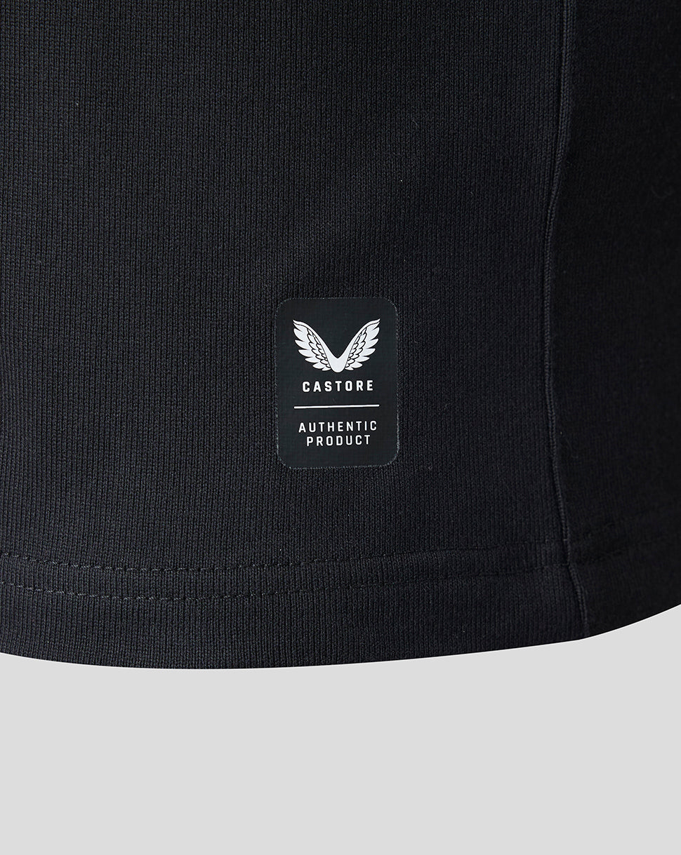 Close-up of a black ribbed knit garment showing a small rectangular Castore patch with a winged logo and the words 'AUTHENTIC PRODUCT' on a light gray background.