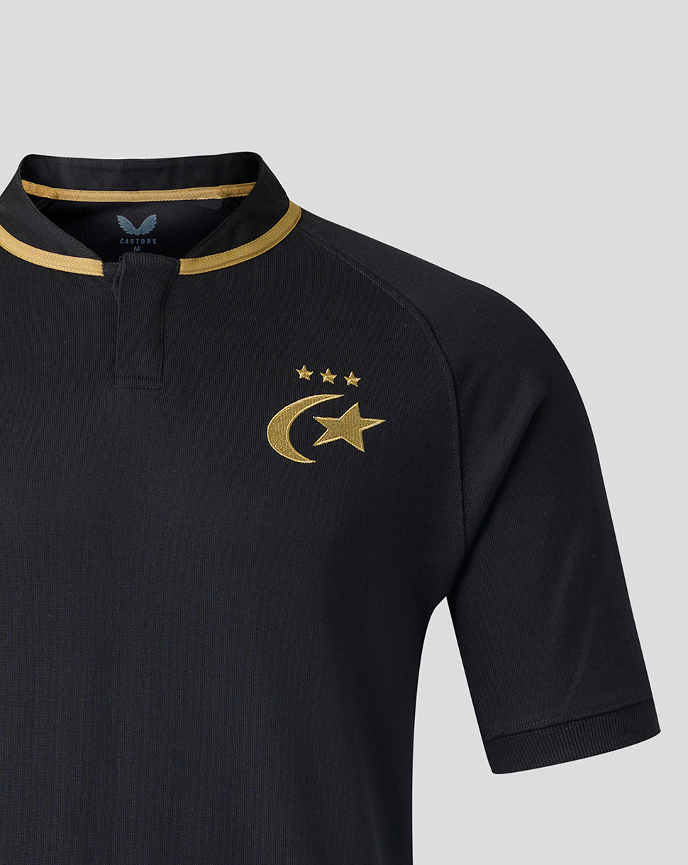 Close-up of a black short-sleeve polo shirt with gold trim on the collar and a gold crescent and star emblem with three stars on the chest, shown on a light gray background.