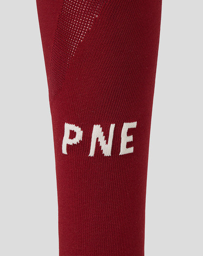 A close-up of a red knit athletic sock featuring the white letters 'PNE' knitted onto the side, set against a solid light gray background.