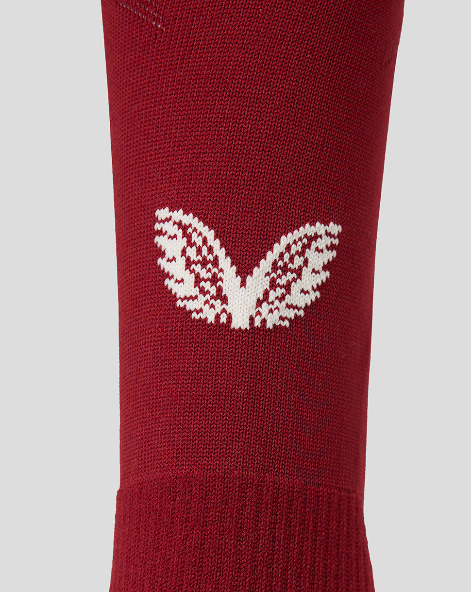 A close-up of a red knit sock featuring a white knit Castore logo on the side, set against a solid light gray background.