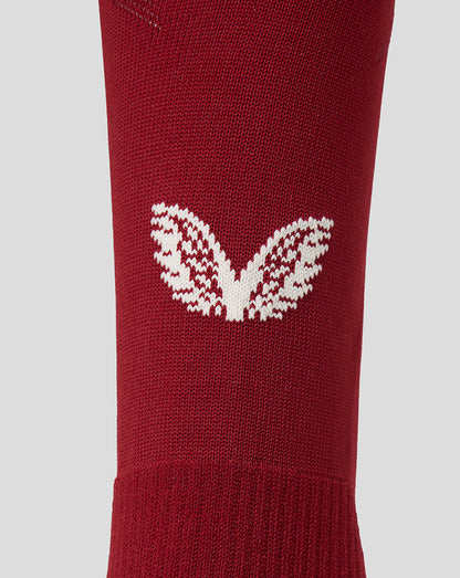 A close-up of a red knit sock featuring a white knit Castore logo on the side, set against a solid light gray background.