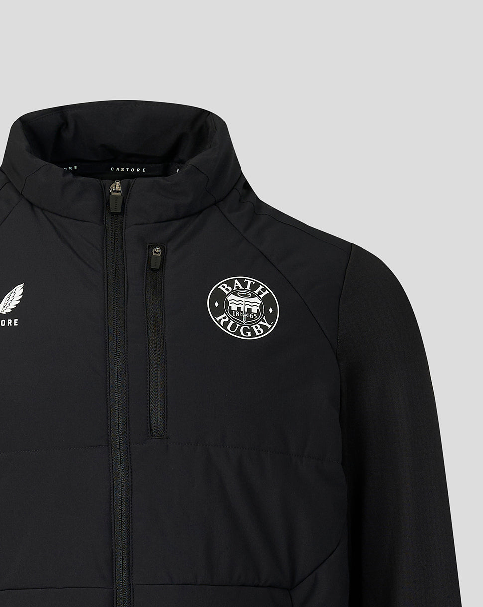 A close-up of a black zip-up jacket featuring a white circular 'Bath Rugby' crest on the left chest and a white winged logo on the right chest, set against a solid light gray background.