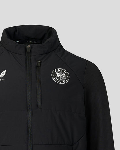 A close-up of a black zip-up jacket featuring a white circular 'Bath Rugby' crest on the left chest and a white winged logo on the right chest, set against a solid light gray background.
