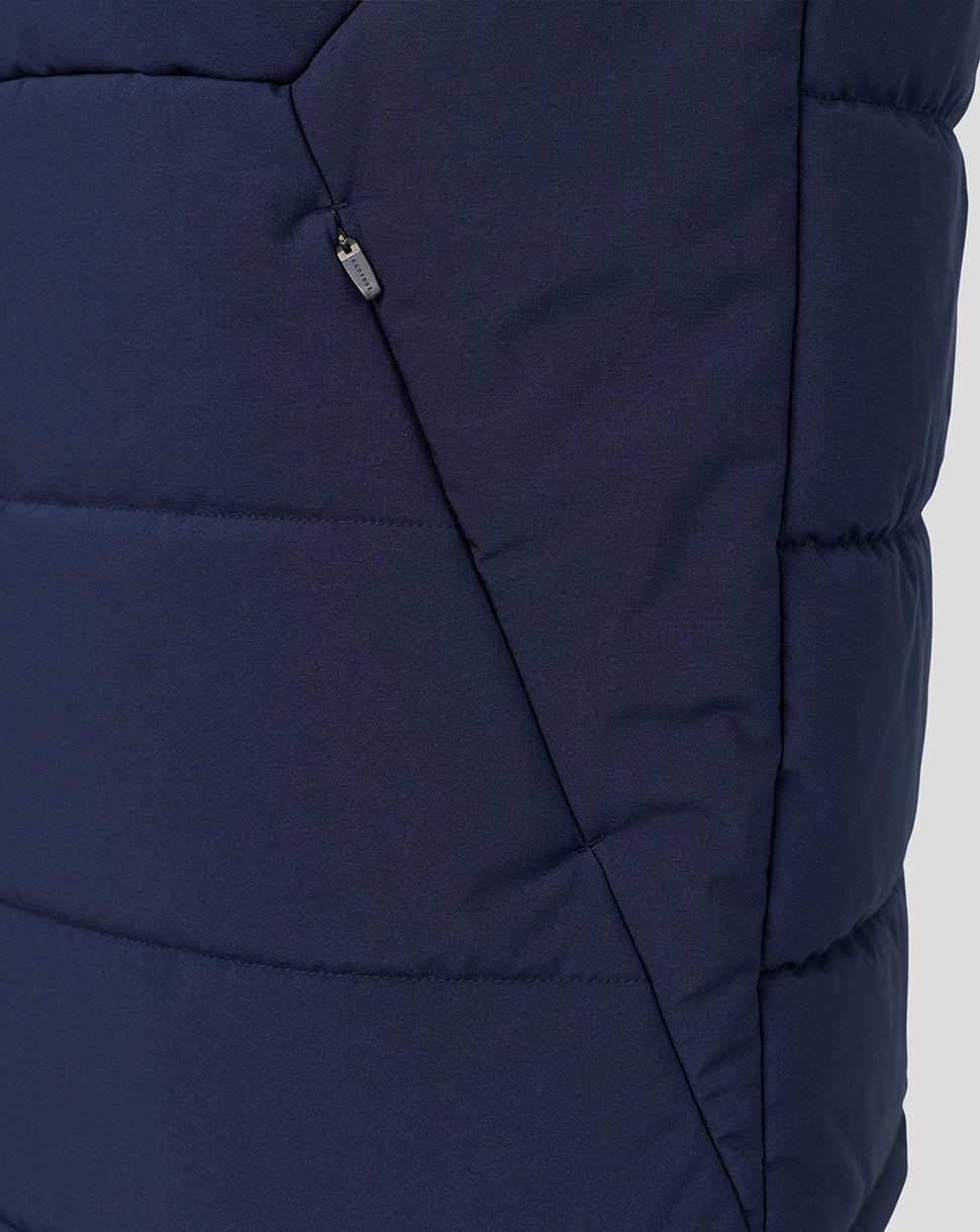 Close-up of a navy blue puffer vest showing the quilted texture, diagonal seam, and a small silver zipper pull.
