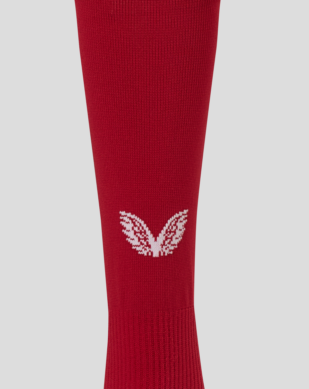 A close-up of a red ribbed knit sock featuring a white embroidered wing logo near the lower calf, set against a solid light gray background.