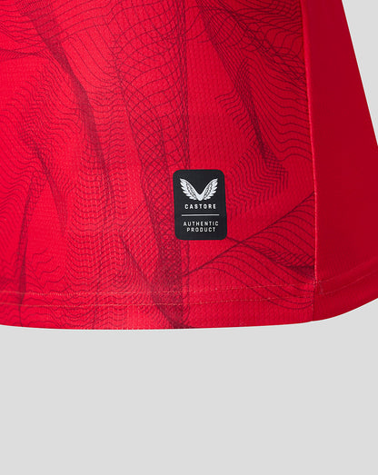 Close-up of a red athletic garment with a subtle tonal topographic pattern and a black Castore Authentic Product label sewn onto the side.
