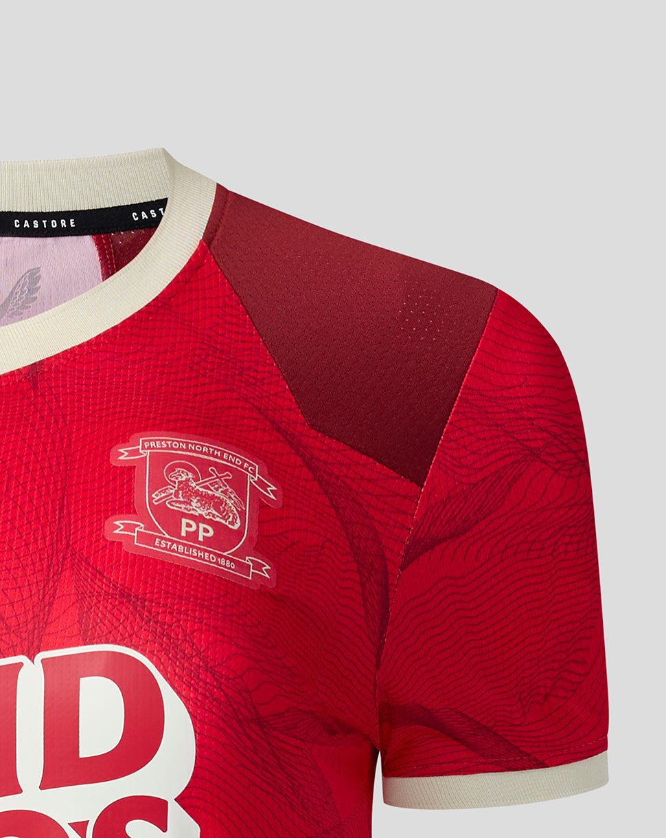 Close-up of a red sports jersey with a textured pattern, cream ribbed collar and cuffs, and a white crest on the chest.
