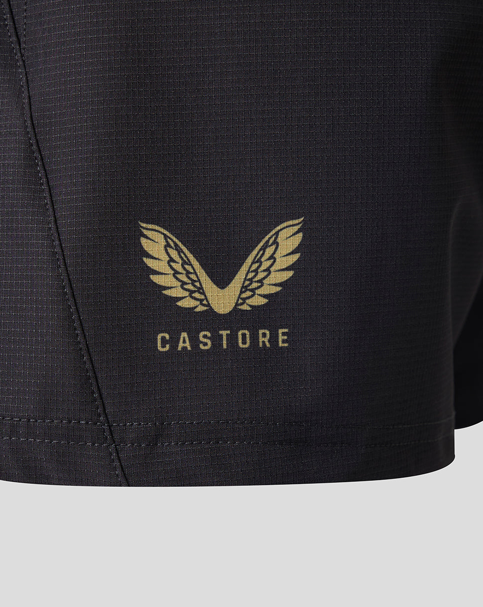 Close-up of a black athletic shorts leg featuring a gold Castore wing logo and brand name printed on the front.