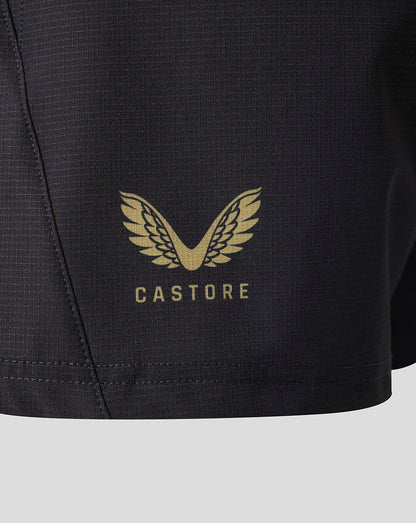 Close-up of a black athletic shorts leg featuring a gold Castore wing logo and brand name printed on the front.