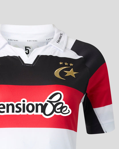 A close-up of a short-sleeve sports jersey with horizontal black, red, and white stripes, featuring a gold crescent and star logo with three stars on the chest. The sponsor 'Pension Bee' is printed across the red stripe, and the brand 'Stinetz' is visible on the collar.