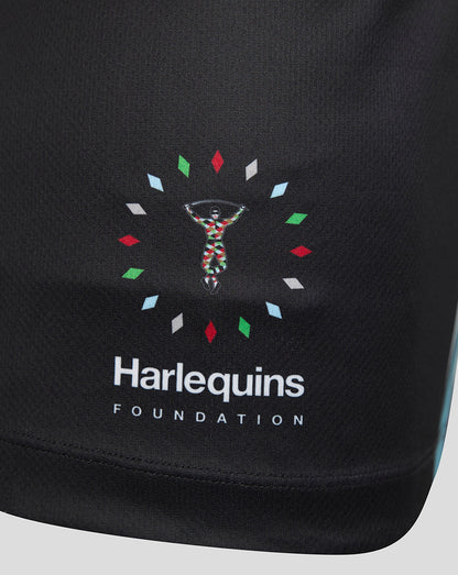 Close-up of a black athletic garment featuring the Harlequins Foundation logo printed on the front. The logo includes a colorful figure surrounded by small multicolored diamond shapes, with 'Harlequins' and 'FOUNDATION' in white text below.