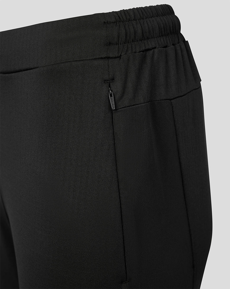 Close-up of black athletic pants showing the elastic waistband, side zip pocket, and front seam against a light gray background.