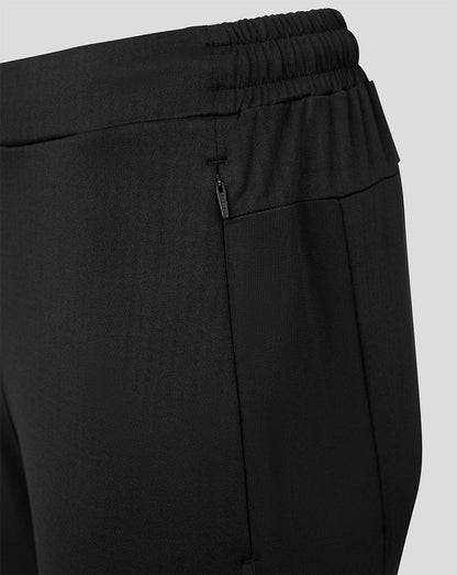 Close-up of black athletic pants showing the elastic waistband, side zip pocket, and front seam against a light gray background.