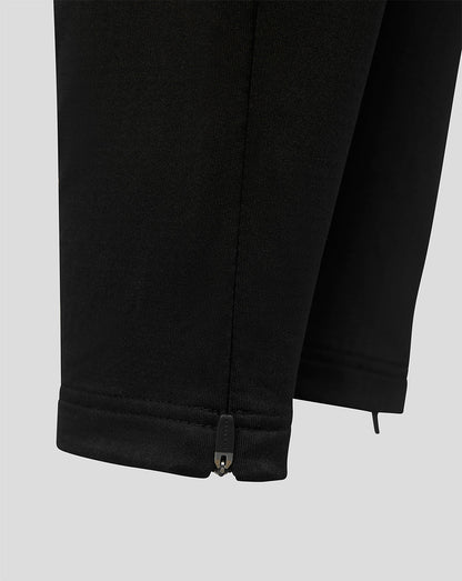 Close-up of black pants showing the hem with a small metal zipper pull tab, on a light gray background.