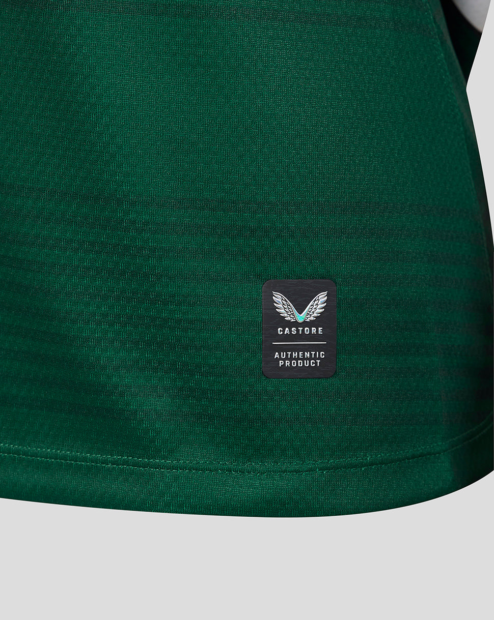 Close-up of a dark green athletic fabric with a small black rectangular patch featuring a white winged logo and the text 'CASTORE AUTHENTIC PRODUCT'.