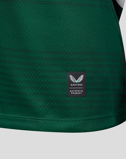 Close-up of a dark green athletic fabric with a small black rectangular patch featuring a white winged logo and the text 'CASTORE AUTHENTIC PRODUCT'.