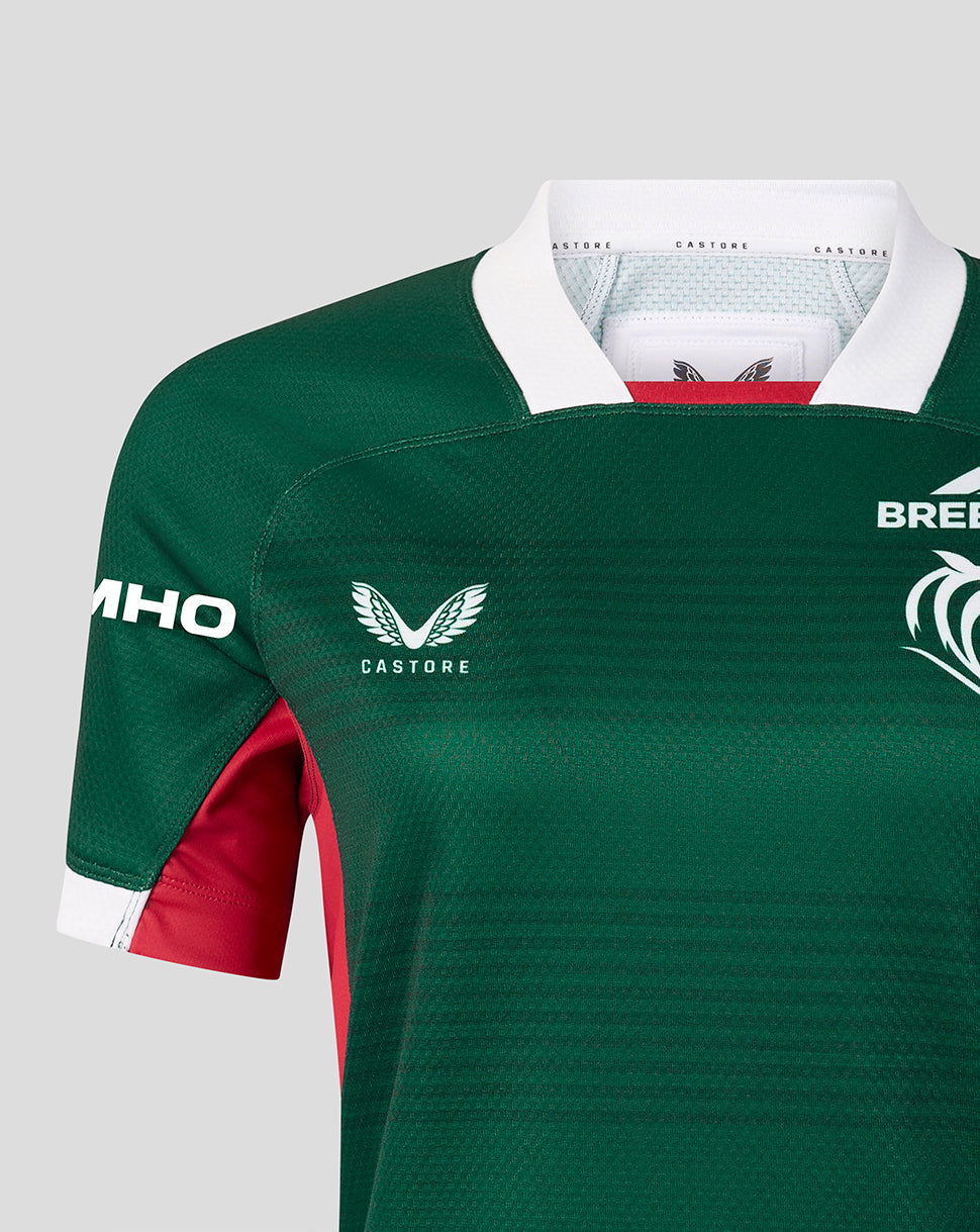 Close-up of a green Castore rugby jersey with white collar and sleeve trim, red side panels, and white logos including the Castore wing logo and Bree Rugby crest.