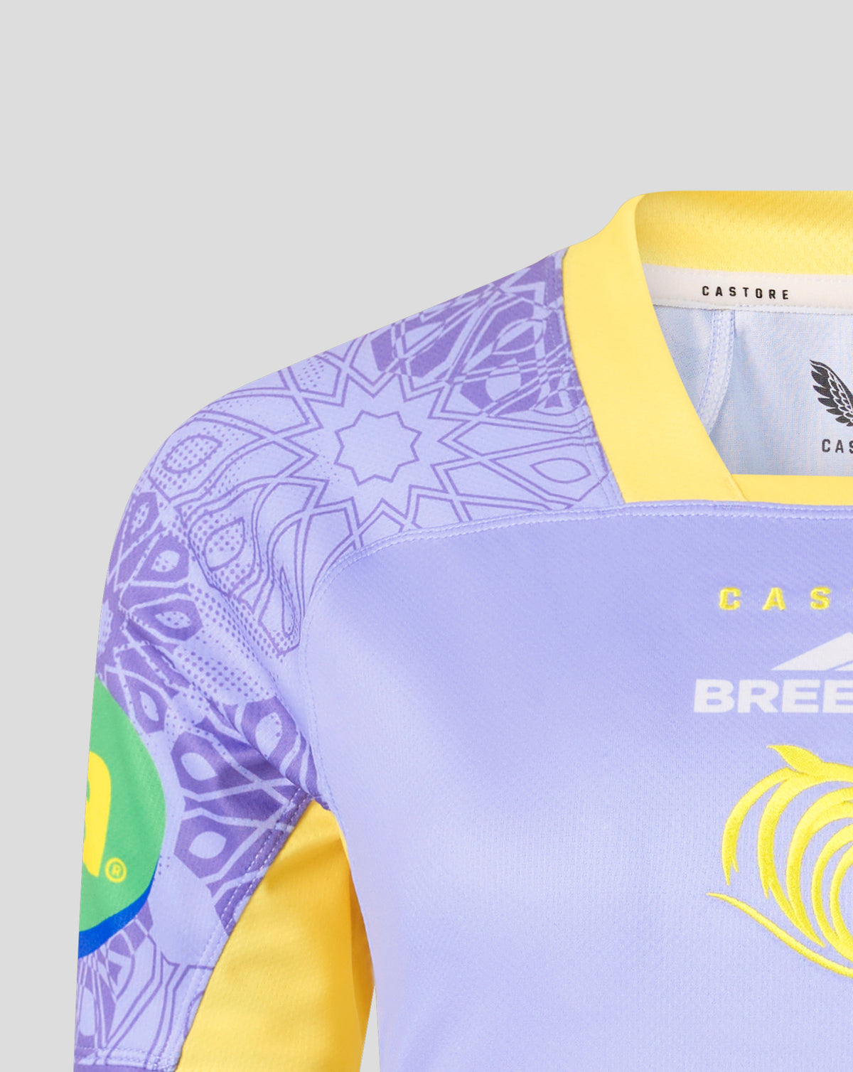 Close-up of a light purple and yellow athletic jersey with a purple mandala pattern on the sleeve, a yellow collar, and yellow branding on the chest.