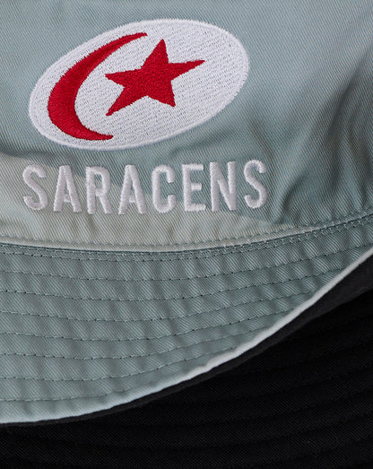 Close-up of teal fabric with a white circular patch showing a red crescent and star and Saracens embroidery.