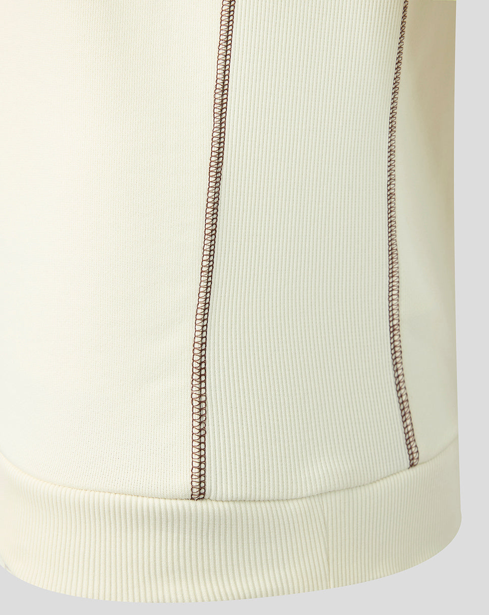 Close-up of a ribbed knit garment in a warm off-white or cream color, showing two vertical decorative contrast stitches and a matching ribbed hem.