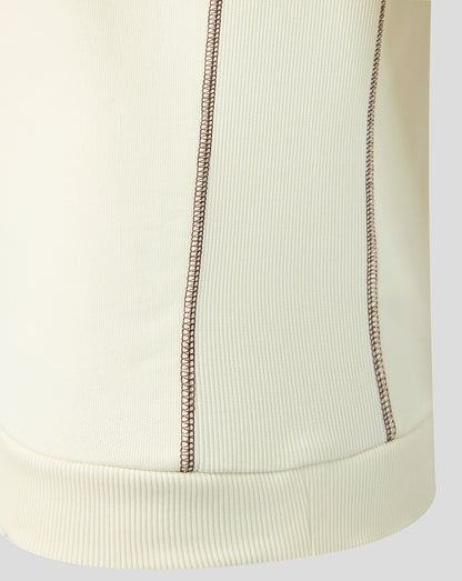 Close-up of a ribbed knit garment in a warm off-white or cream color, showing two vertical decorative contrast stitches and a matching ribbed hem.