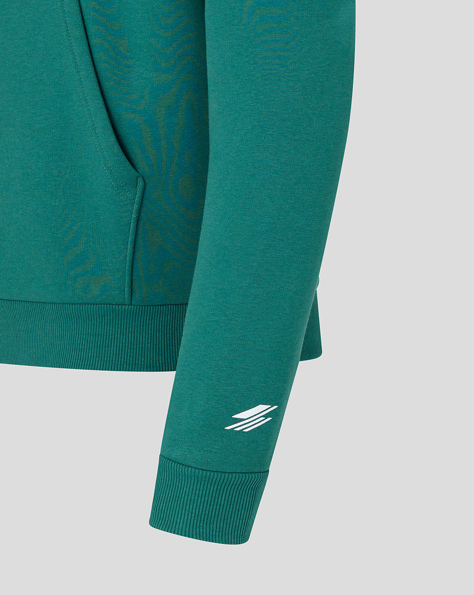 Close-up of a teal-green long-sleeve hoodie with a subtle tonal pattern on the body and a white stylized logo on the sleeve cuff, shown against a light gray background.