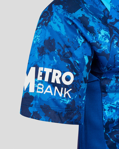 Close-up of the sleeve showing the Metro Bank logo on blue camouflage cricket jersey fabric.