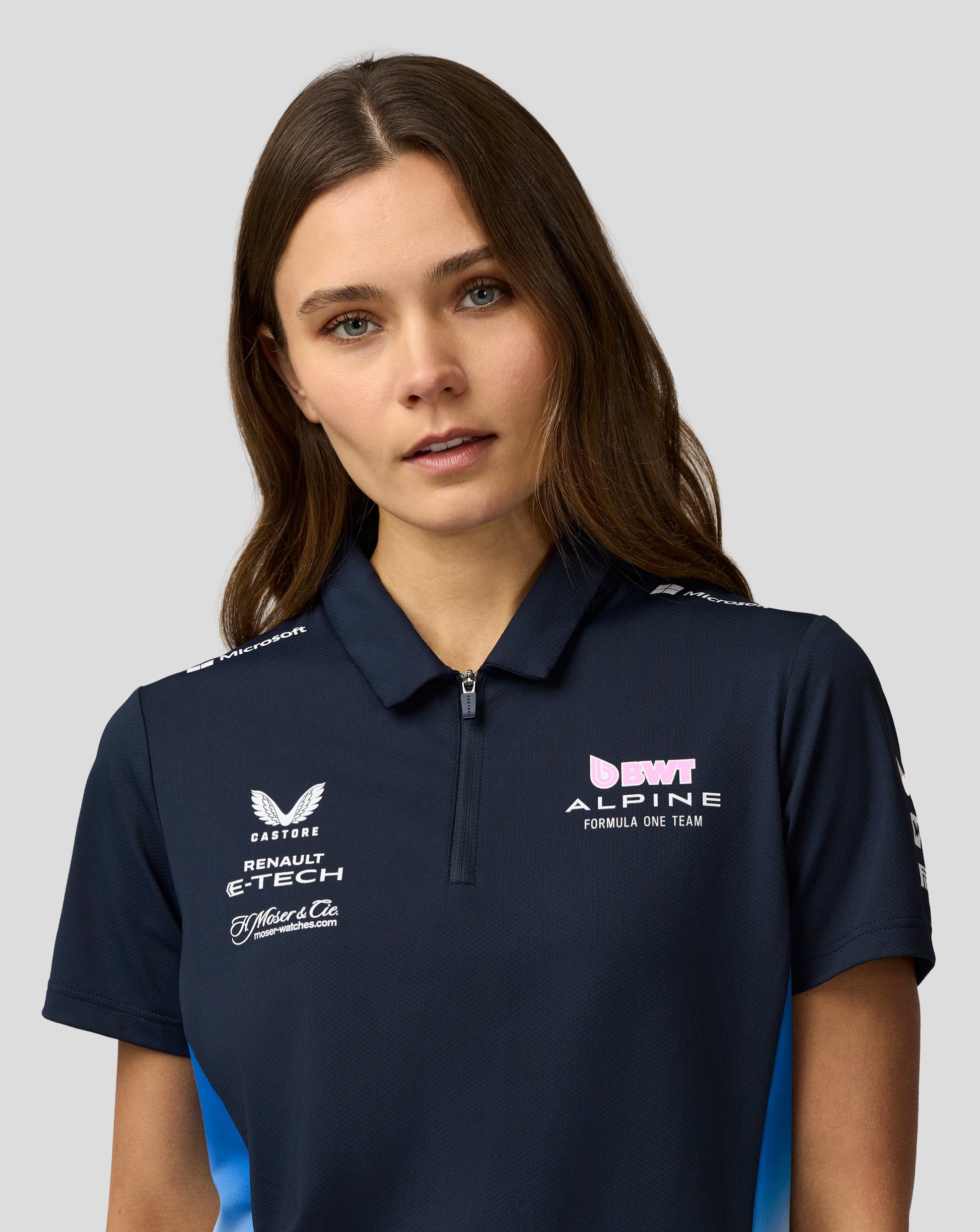 Close up of a woman in a navy polo with center zip and Alpine team logos on the chest