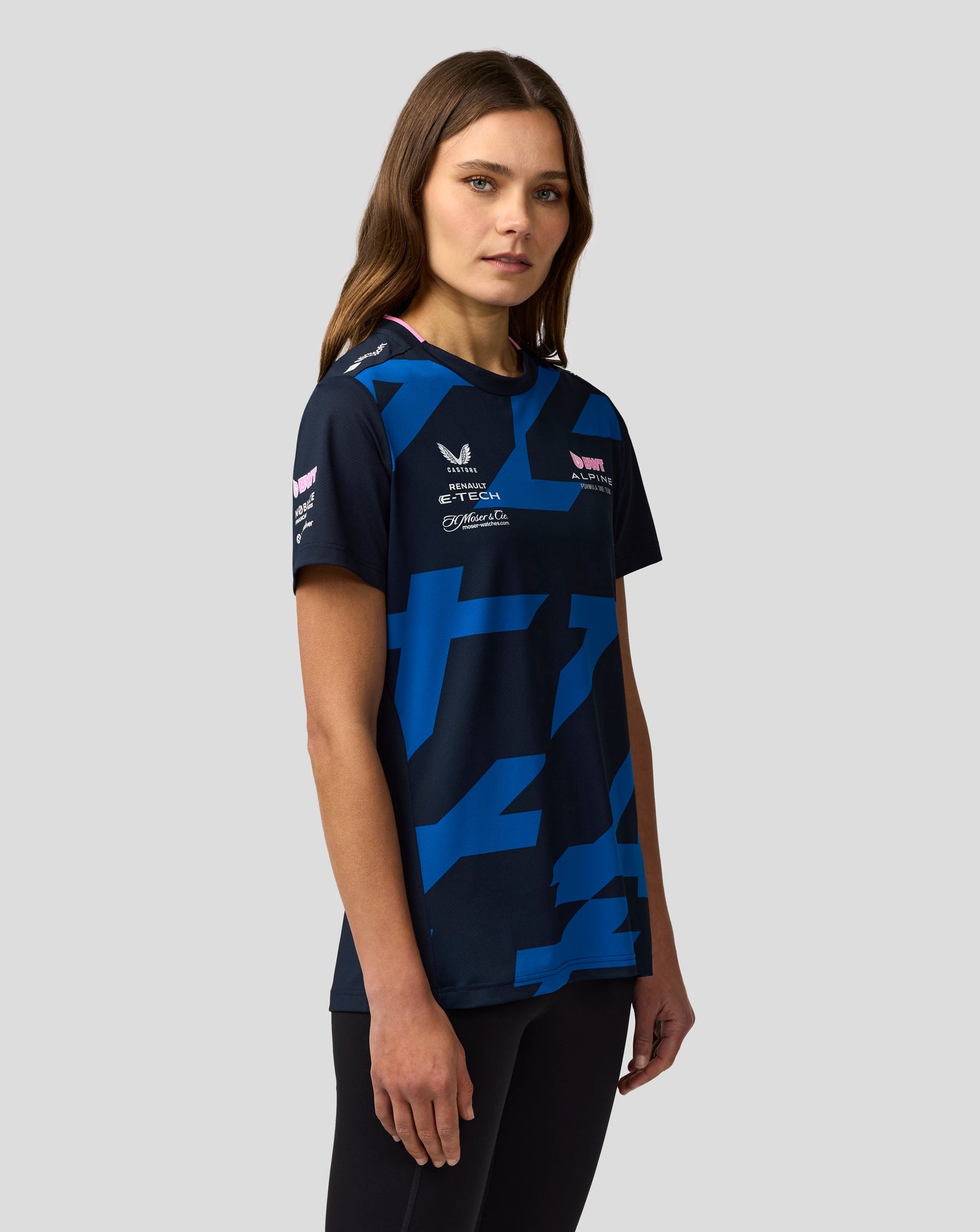 Side profile of a woman wearing navy Alpine F1 Team Jack Doohan jersey with blue geometric print and sponsor logos
