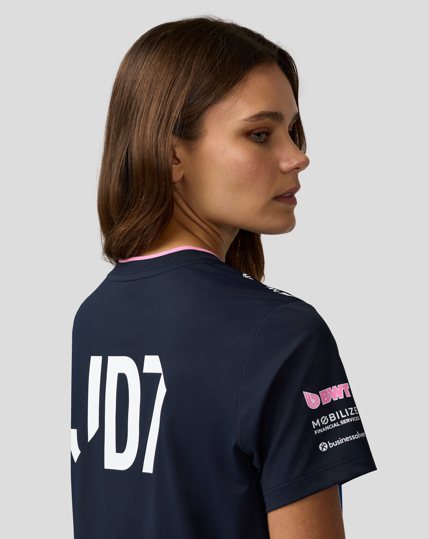 Profile of a woman wearing a navy Alpine Formula One Team jersey with blue stripes and bold white lettering on the back.
