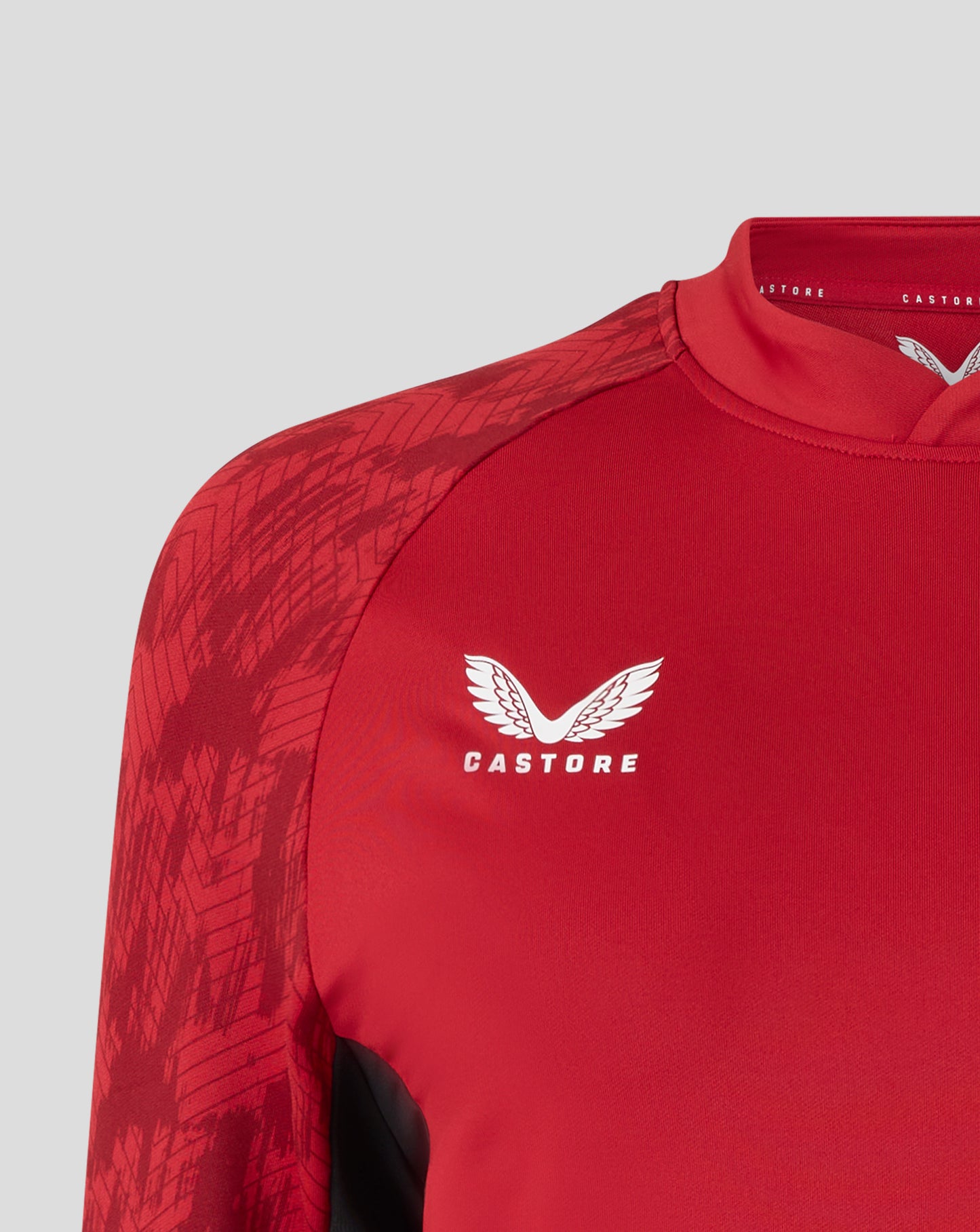 Close-up of Saracens training drill top in Rhythmic Red with a patterned shoulder panel and subtle logo.