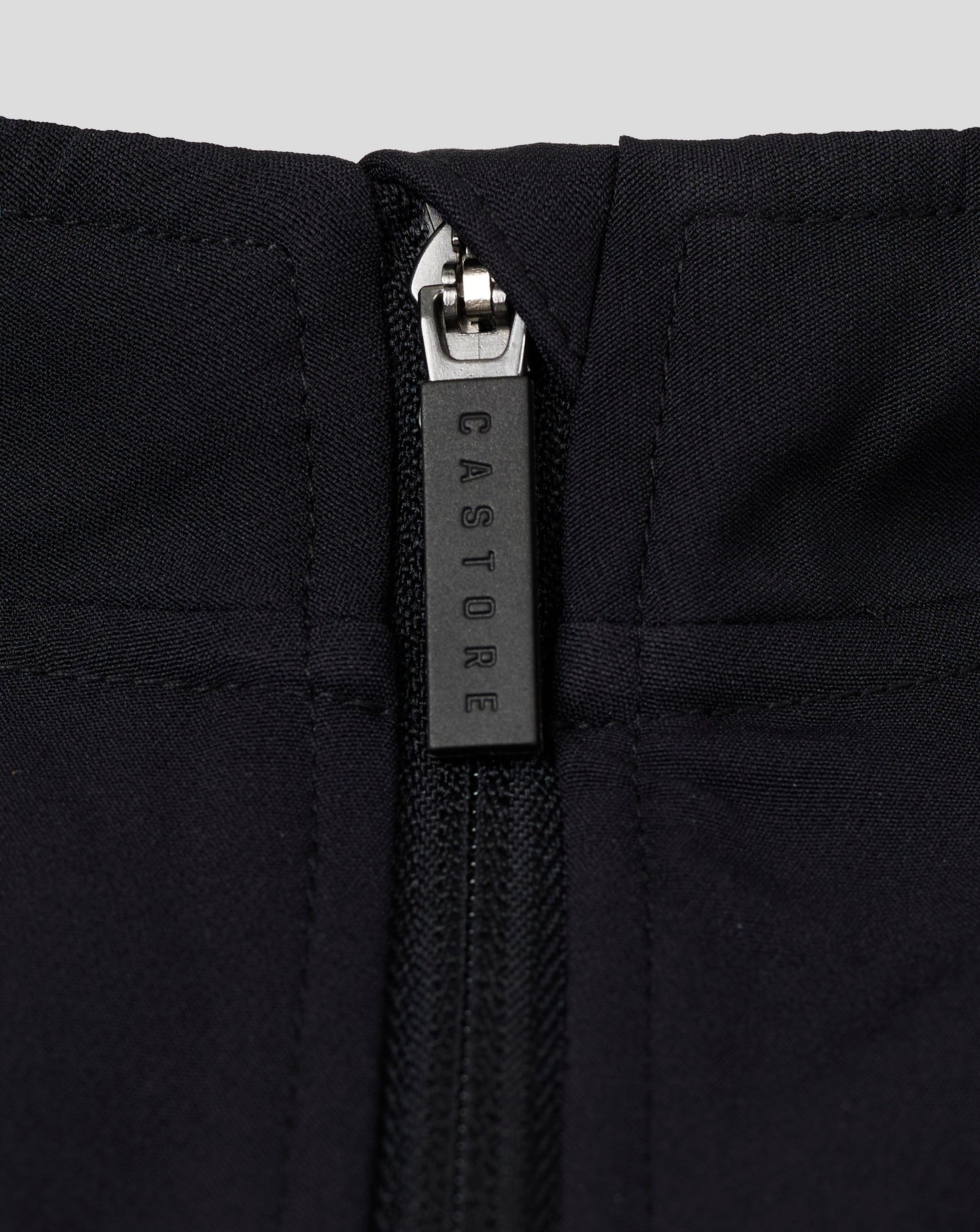 Close up of the zipper on a black womens track jacket at the funnel neck with quilted panels