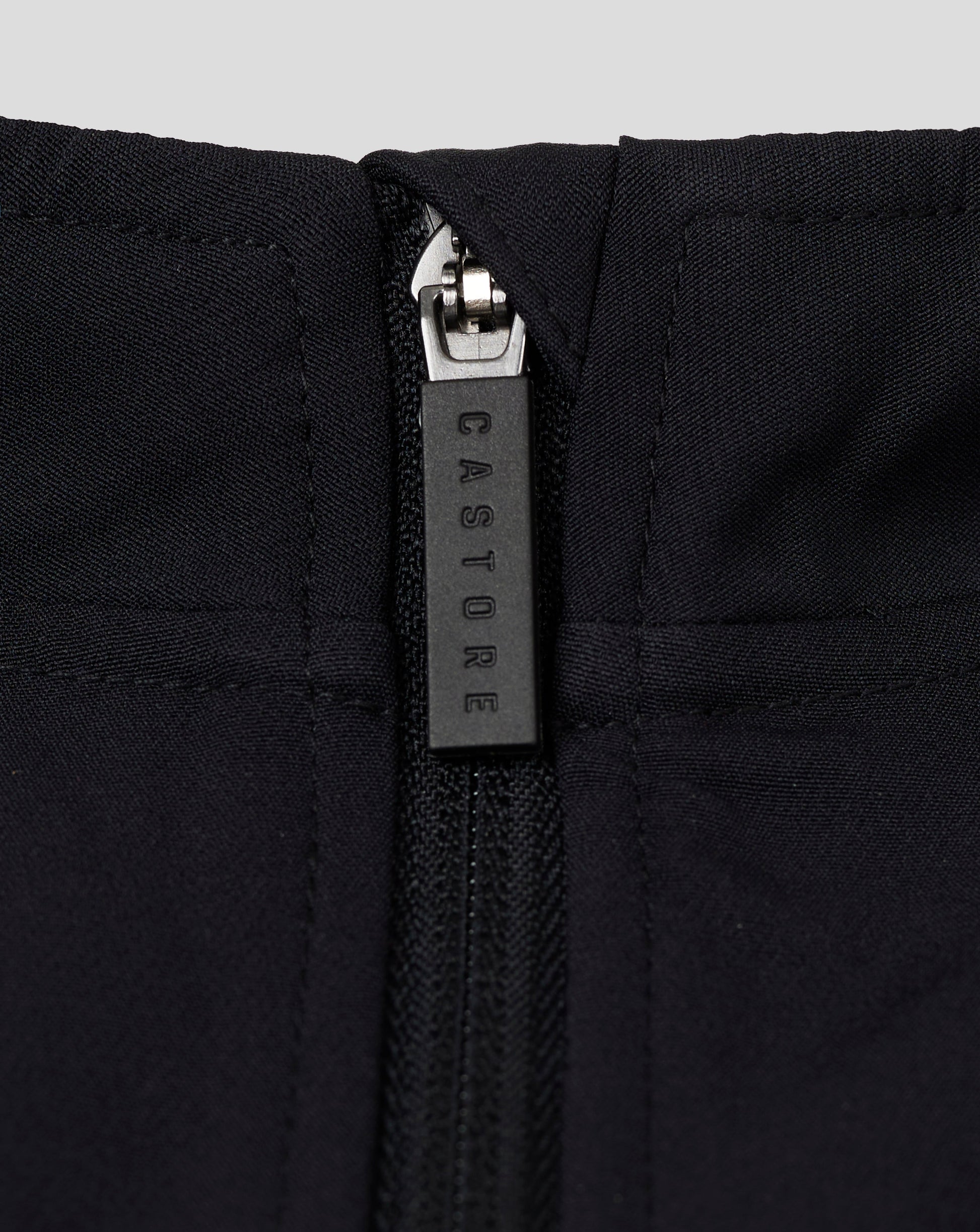 Close up of the zipper on a black womens track jacket at the funnel neck with quilted panels