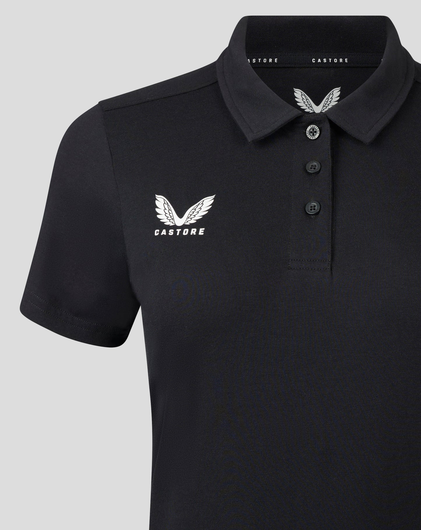 Front close up of black polo showing self fabric collar three button placket and white Castore logo on chest.