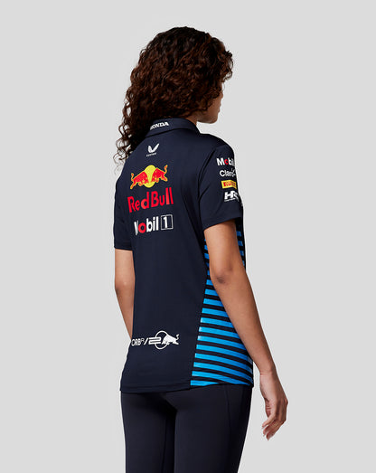Back view of female model in navy Night Sky Teamline polo with large Red Bull logo and sponsor badges on the back and blue striped sides.