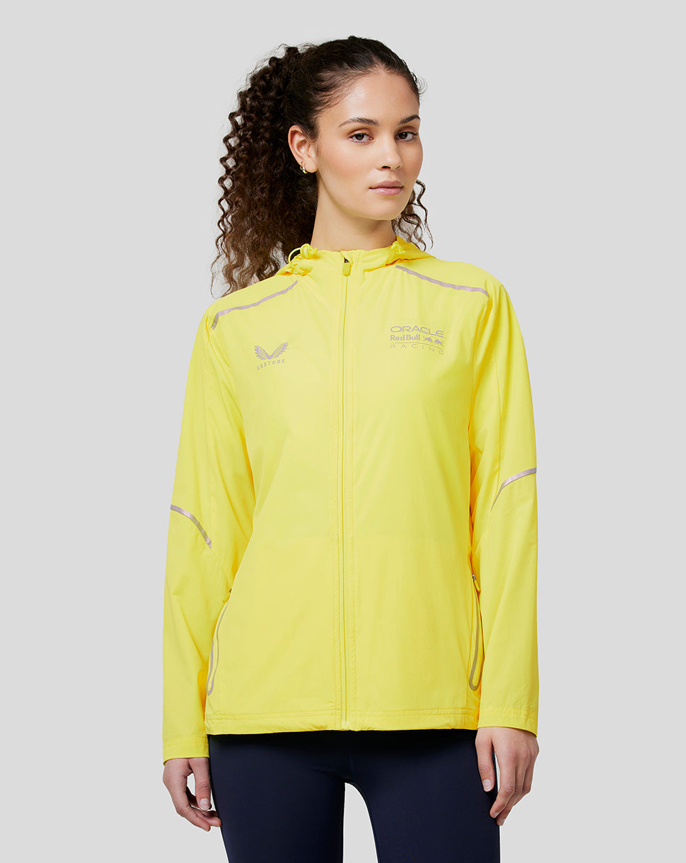 Front view of a woman in a bright safety yellow Oracle Red Bull Racing windbreaker with zip pockets and reflective details