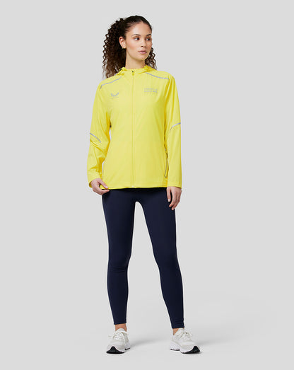 Model wears Oracle Red Bull Racing Womens Active Dual Brand Wind Breaker in safety yellow with reflective detailing and zipped pockets.