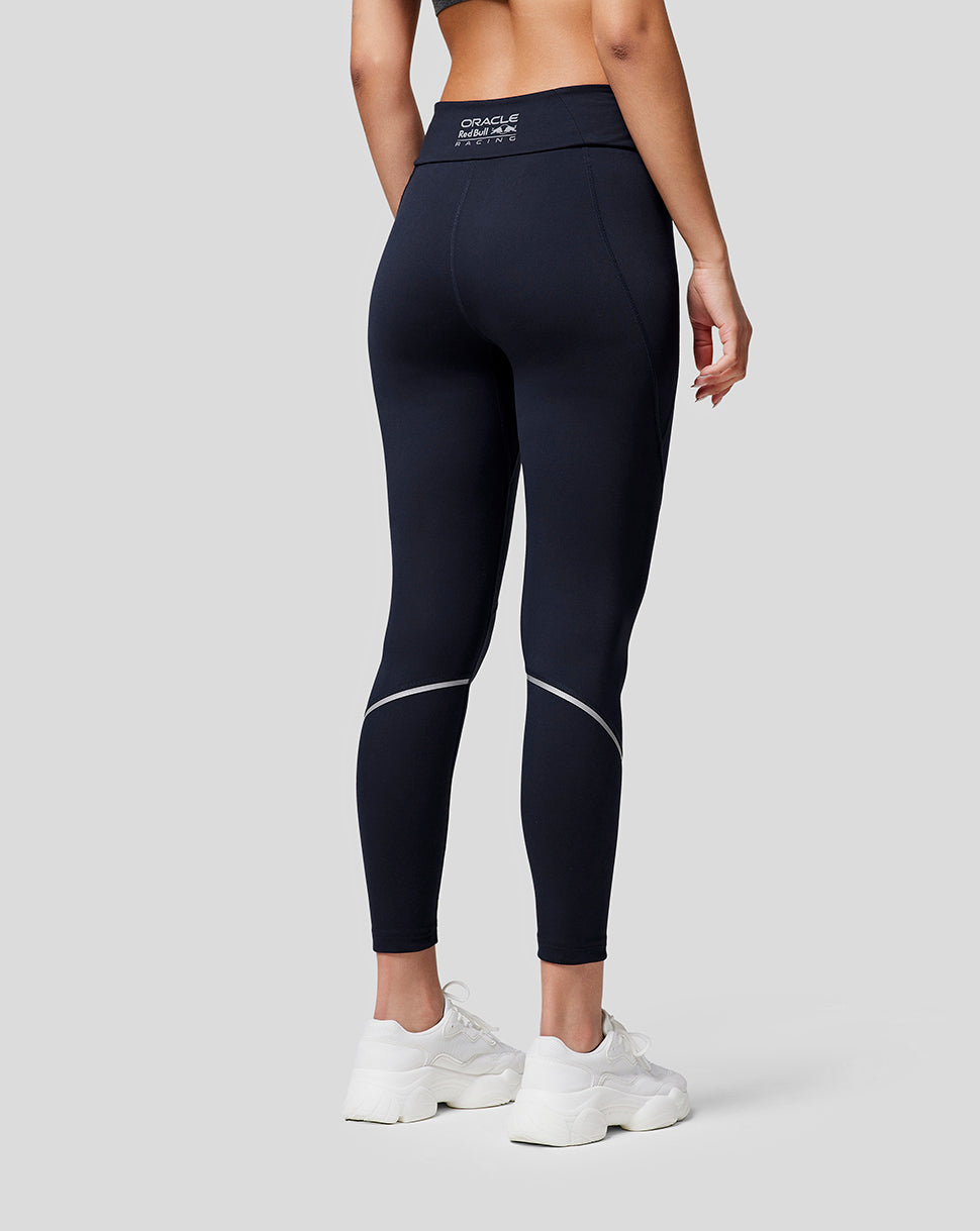 Back view of a model wearing navy Oracle Red Bull Racing running leggings with contour seams and reflective details, white sneakers.
