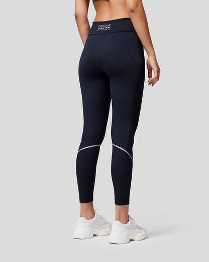 Back view of a model wearing navy Oracle Red Bull Racing running leggings with contour seams and reflective details, white sneakers.