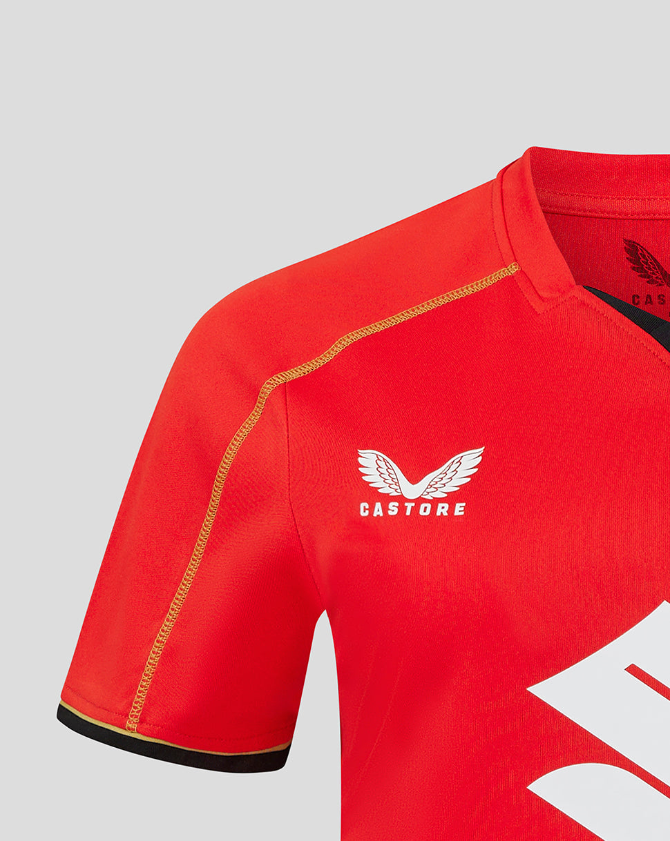Red Mk Dons away shirt close up showing white Castore logo and gold crest on the chest.