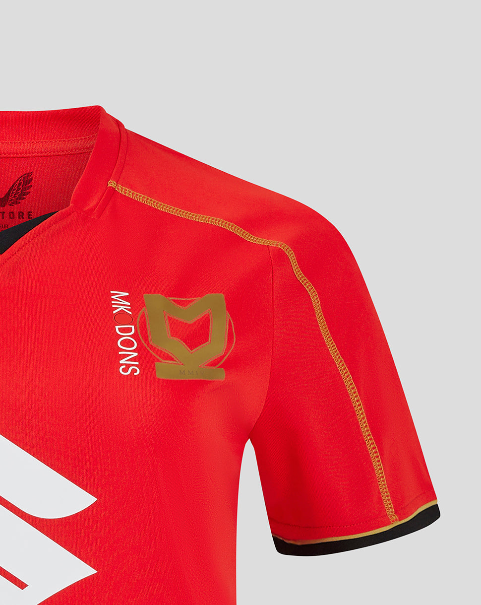 Red Mk Dons away shirt sleeve close up with gold stitched seam and a gold crest on the chest area.