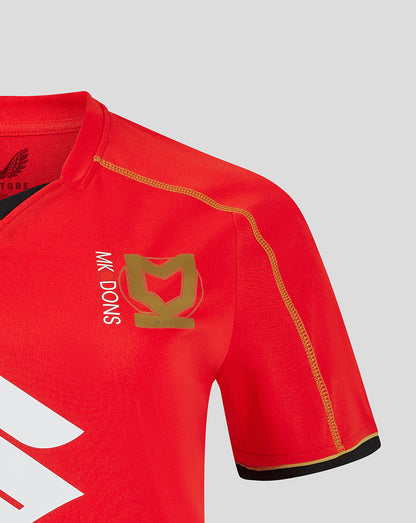 Red Mk Dons away shirt sleeve close up with gold stitched seam and a gold crest on the chest area.