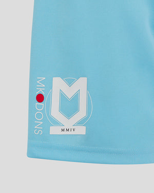 Close up of light blue Mk Dons shorts featuring a large white crest logo on the left leg and vertical Mk Dons text along the side