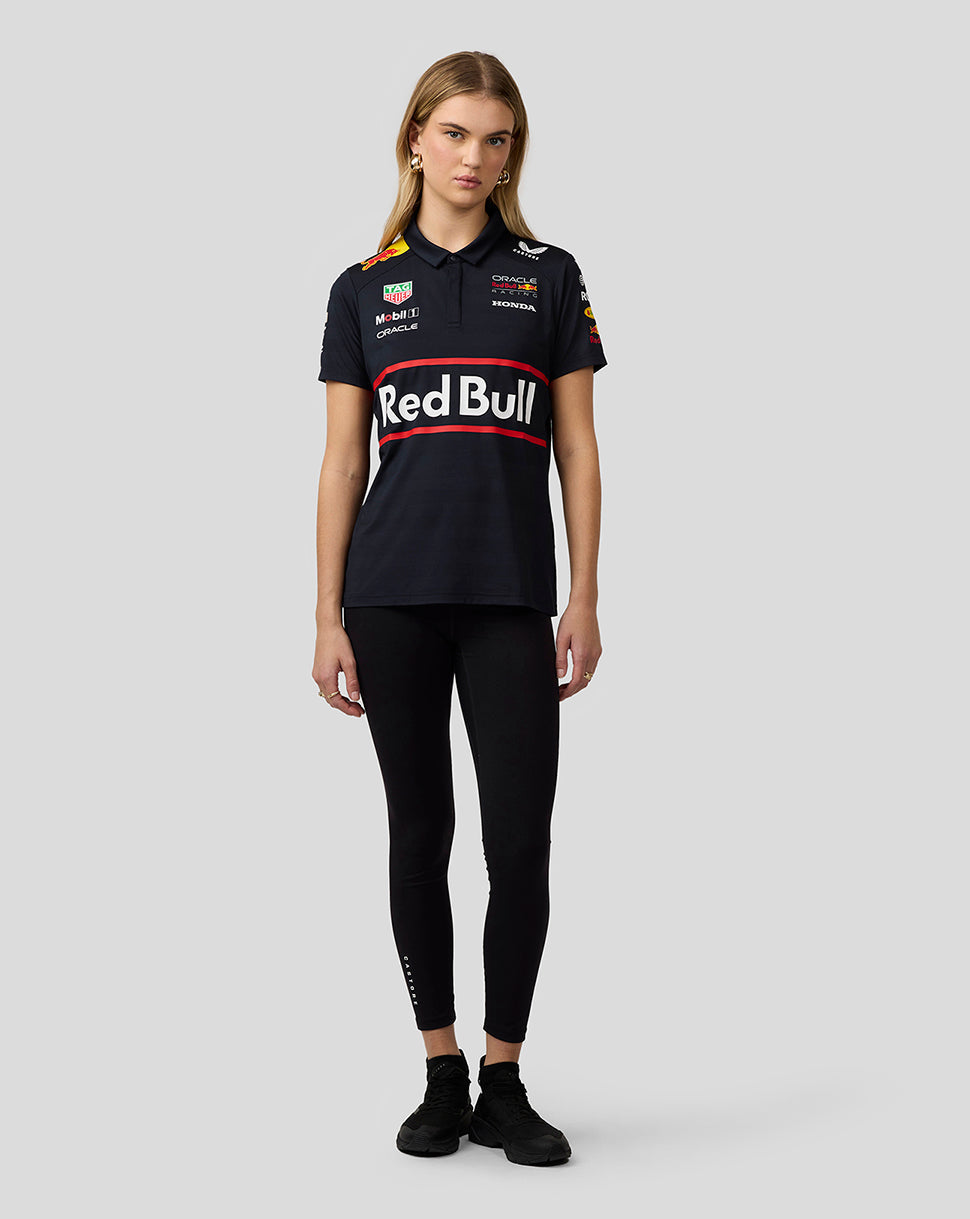 Full body front view of a woman in a navy Red Bull Racing polo with large Red Bull across the chest