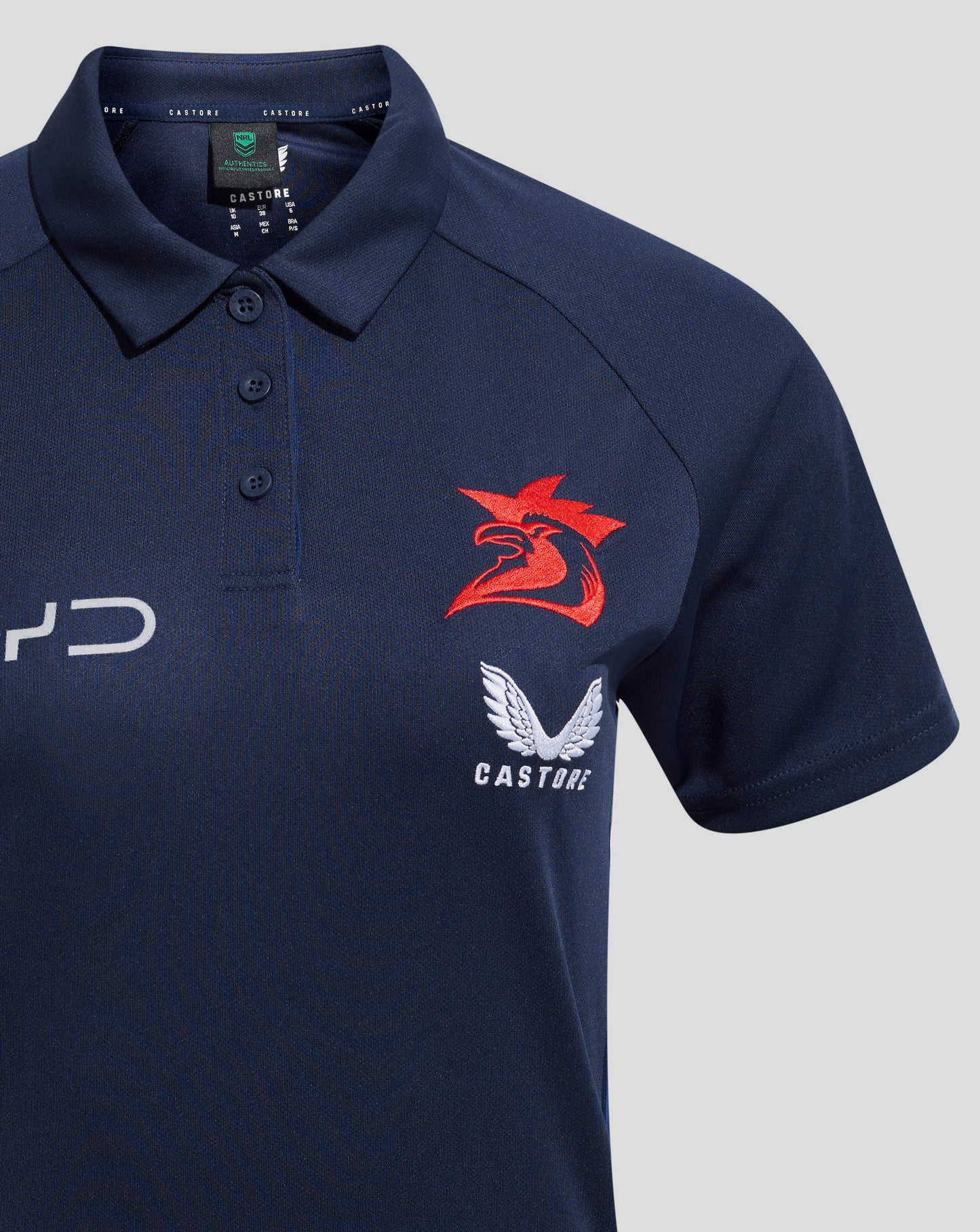 Chest area of navy polo showing a red rooster crest with white wings and Castore branding inside the collar.